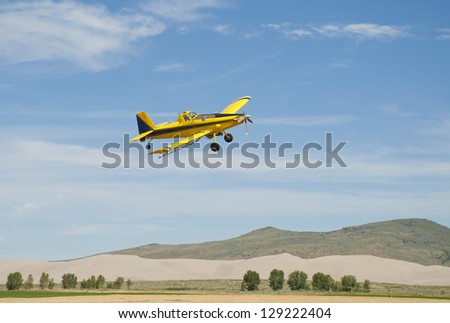 A spray plane flies over a farm and fields on the High Desert of Idaho.
