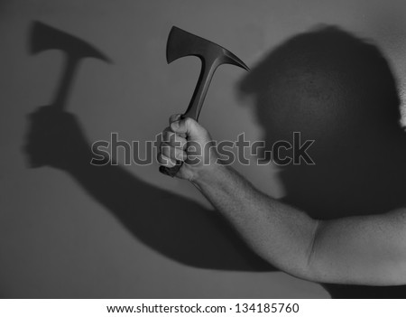 A black and white, high contrast take of a shadowed figure wielding a tomahawk in a downward stroke.