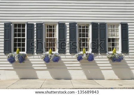 Shuttered windows decorated with flowers and plants in the wall of an eighteenth century house.