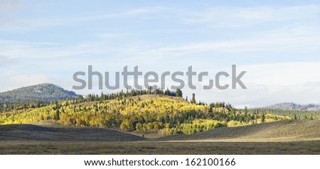 A panoramic view of the snowy mountains and blazing fall colors that adorn the mountains, aspens, and sagebrush steppe of the Wyoming Rocky Mountains.