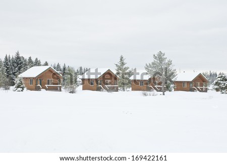 A line of small cabins in the pines are covered in a winter mantle of snow.