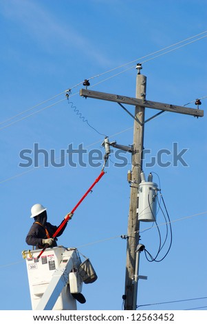 Power lineman in a lift disconnecting a breaker fuse from a power line and transformer.