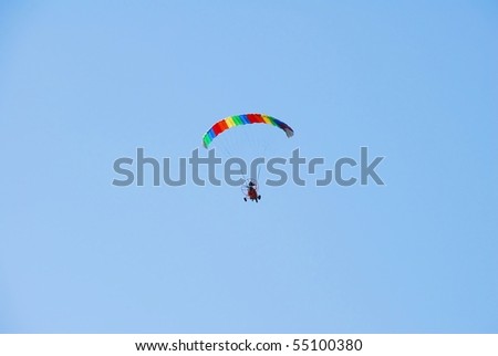 A powered parachuted looks suspended as it flies through a blue sky.