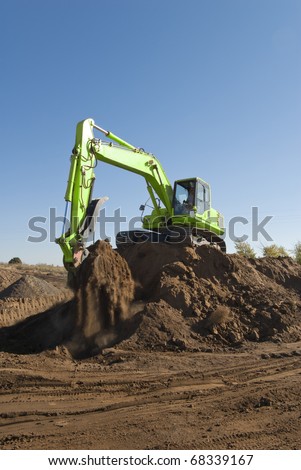 A track hoe on a mound of dirt grabs a scoop of earth.