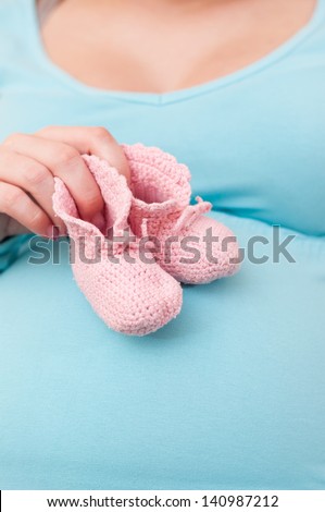 Pregnant Woman (mother) Holding Pink Baby Shoes on her belly.