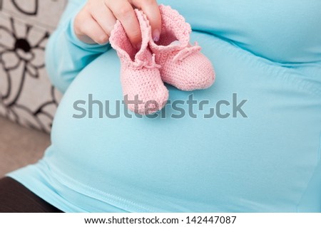 Pregnant Woman (mother) Holding Pink Baby Shoes on her belly.