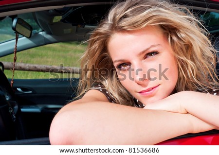 young adult blonde woman leaning on red car