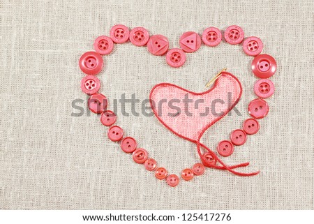 Pink buttons in form of the heart and needle with thread on light fabric