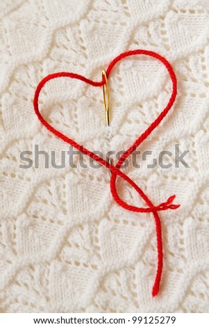 The red thread in the needle in the shape of a heart on a white knitted fabrics
