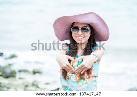 A portrait of beautiful asian woman show hand gesture heart shape on the sea background