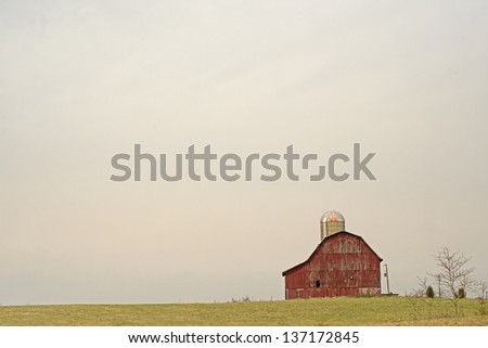 A lone red barn stands alone under an overcast sky.