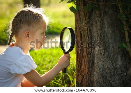 Little girl examining the tree stem through the magnifying glass outdoors