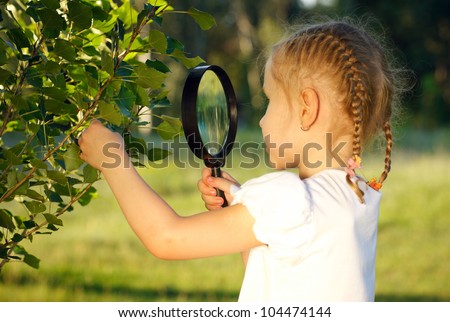 Little girl examining the tree leaves through the magnifying glass outdoors