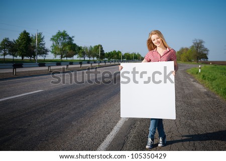 Full length of young beautiful female standing near the road and holding a blank whiteboard