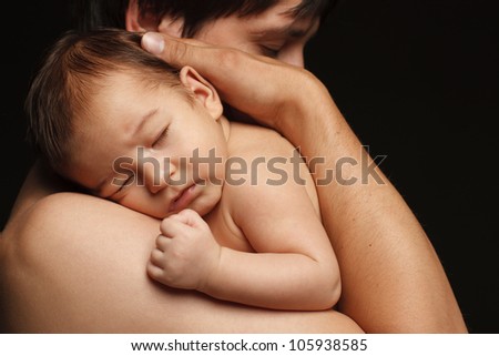 Closeup of sleeping newborn baby in the embraces of his father over black background