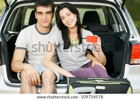 Young smiling couple sitting in the opened car bloom holding empty credit cards