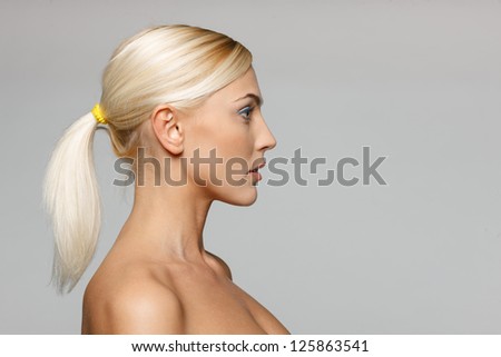 Side view closeup of beautiful blond woman looking forward over gray background