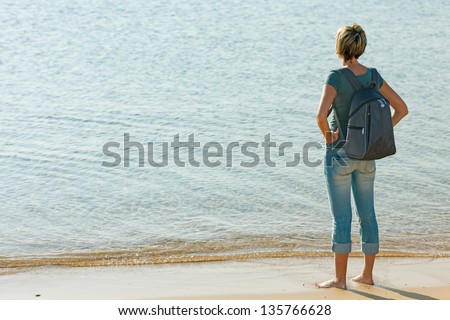Back view of a woman with backpack in full length standing enjoying seascape