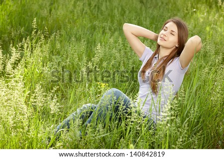 Relaxing woman sitting in grass enjoying fresh air with hands clasped over her head