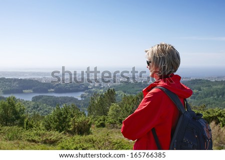 Woman with backpack enjoying valley city view from top of a mountain