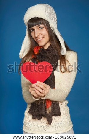 Winter girl, young beautiful girl in hat and muffler giving  over blue background