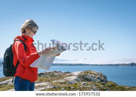 Woman tourist reading the map, during travel in Norway against blue hazy fjord background