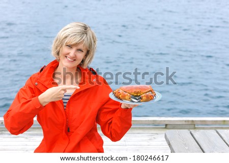 Gourmet eating. Happy woman holding cooked crab on white plate and pointing at it