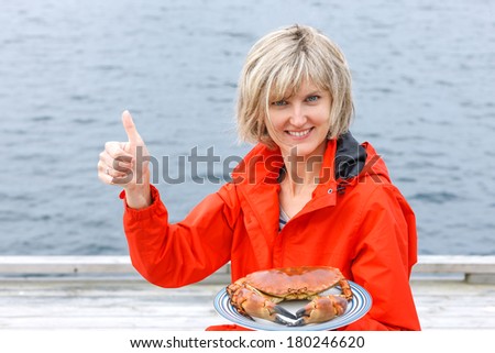 Gourmet eating. Happy woman holding cooked crab on white plate and gesturing thumb up.