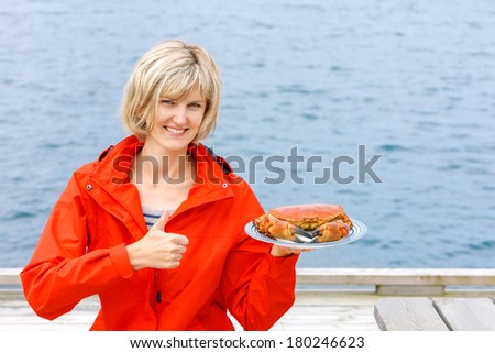 Gourmet eating. Happy woman holding cooked crab on white plate and gesturing thumb up.