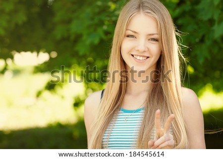 Summer girl portrait.  Closeup of a woman smiling happy on sunny summer or spring day outside in park showing victory or peace sign. Pretty young woman outdoors.