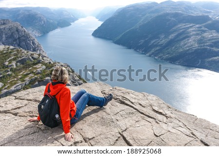 Woman hiker on Pulpit Rock / Preikestolen, Norway enjoying Lysefjorden view.  Pulpit rock is a massive cliff 604 metres above Lysefjorden, almost flat, and is a famous tourist attraction in Norway.