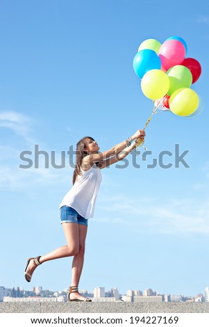 Happy young woman flying away with colorful balloons in full length, urban scene,city view, outdoors