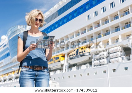 Woman tourist on shore looking at map, standing in front of big cruise liner, summer day