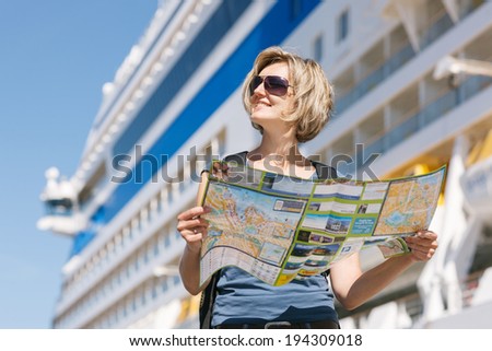 Woman tourist on shore with a map, standing in front of big cruise liner, summer day
