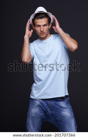 Man fashion model, stylish young man standing posing with hat, over black background