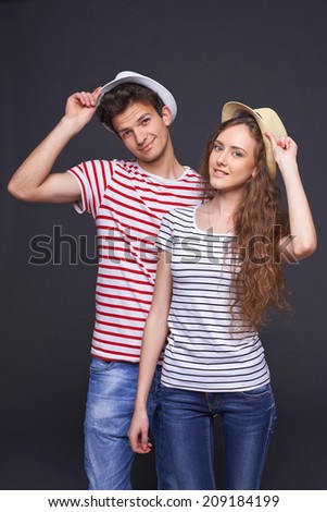 Beautiful young couple in summer hats taking off their straw hats as greeting over gray background