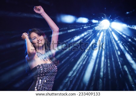 Young woman dancing in club with flashes and disco ball on background