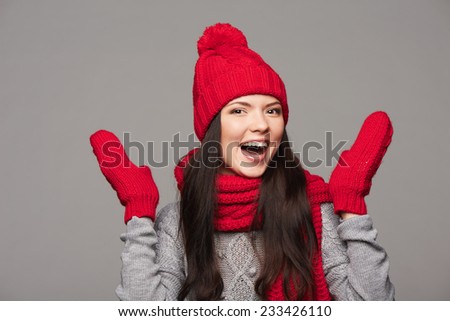 Happy laughing woman wearing red winter hat, scarf and mittens over gray background, with copy space