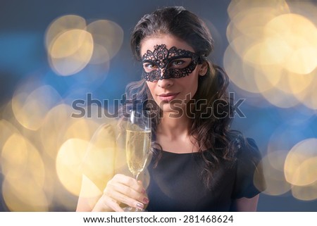 Sensual woman wearing black masquerade carnival mask at party holding a glass with champagne over holiday bokeh background. Closeup portrait with copy space