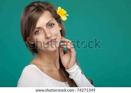 Close-up portrait of young female with flower over the ear on turquoise background