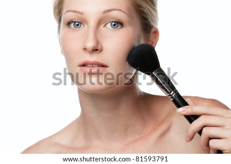 Young beautiful female applying mineral powder with make-up brush isolated on white