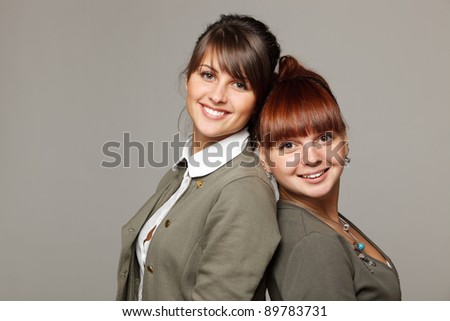 Closeup of two smiling girls standing back to back, over grey background