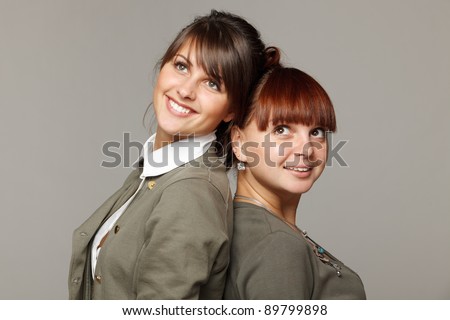 Closeup of two smiling girls standing back to back looking upwards, over grey background