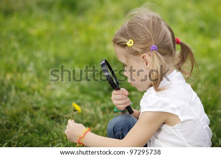 Little girl exploring the flower through the magnifying glass outdoors