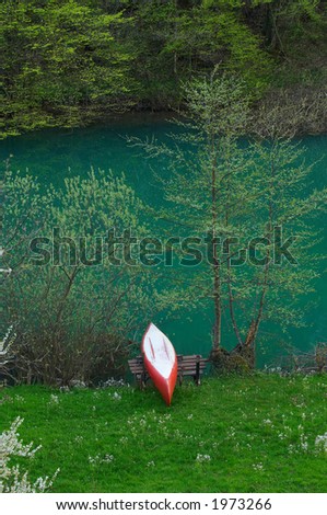 A red and white canoe resting by the green river