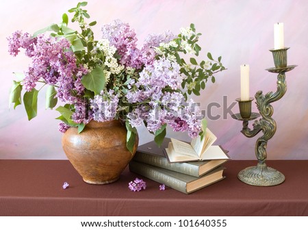 Still life with lilac flowers, books pile, bronze candlestick with candles on painting background