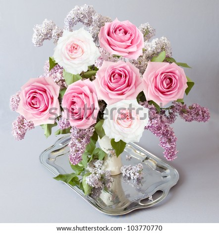 Still life with roses and lilac flowers bunch on silver tea tray on artistic background