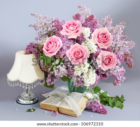 Still life with huge lilac flower and roses bunch with open book,antique pen and lamp on artistic background