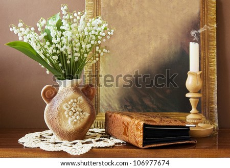 Still life with lily-of-valley bunch in vase, photo album, old painting and candlestick with candle on artistic background
