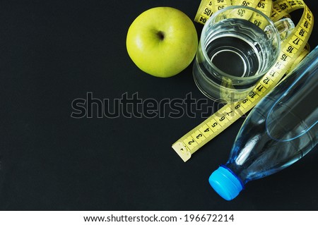 Apple, measuring type and glass of water and bottle on black background.Diet concept